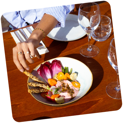 Indulging in Plant-Based Tarama Delight: A hand reaches for a bowl of our exquisite plant-based tarama, adorned with fresh veggies, offering a delectable culinary experience